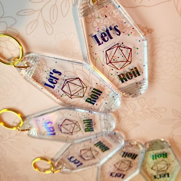 Let's Roll Motel Keychain A confetti glitter style motel keychain with a rainbow Let's Roll with a d20